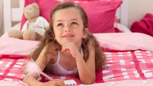 Мечтательная девочка на кровати пишет в блокноте